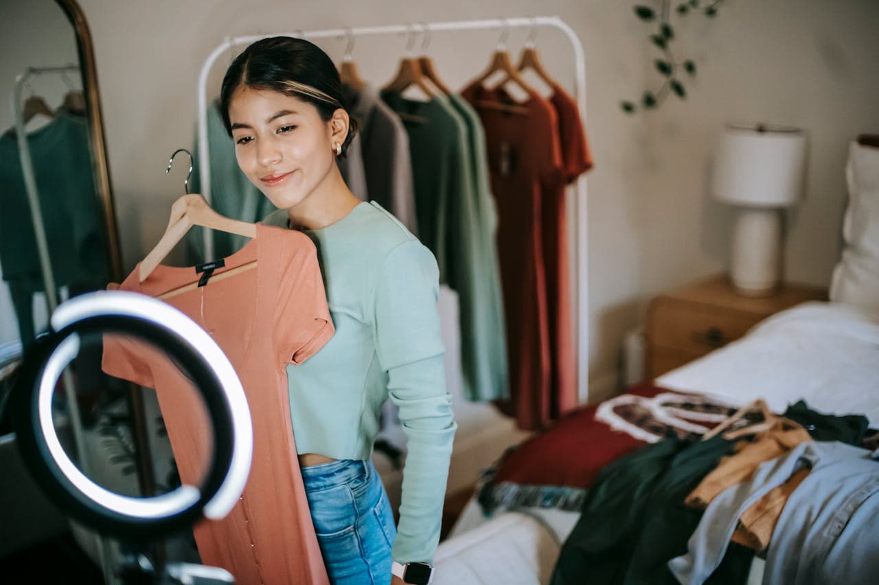 Smiling ethnic woman shooting vlog on phone while demonstrating clothes